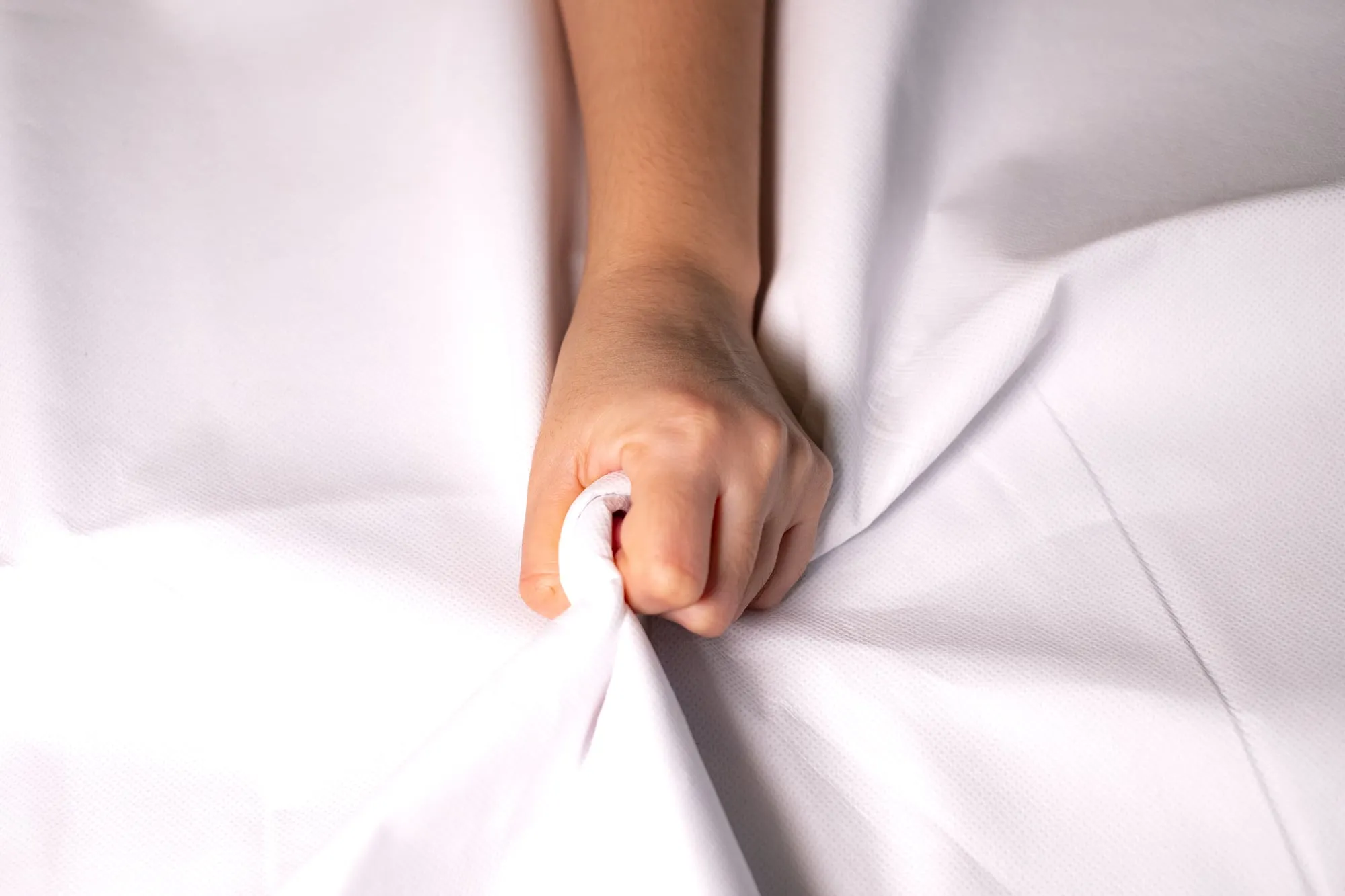 Main de femme serrant des draps blancs, illustrant l'intensité du plaisir lors d'un orgasme